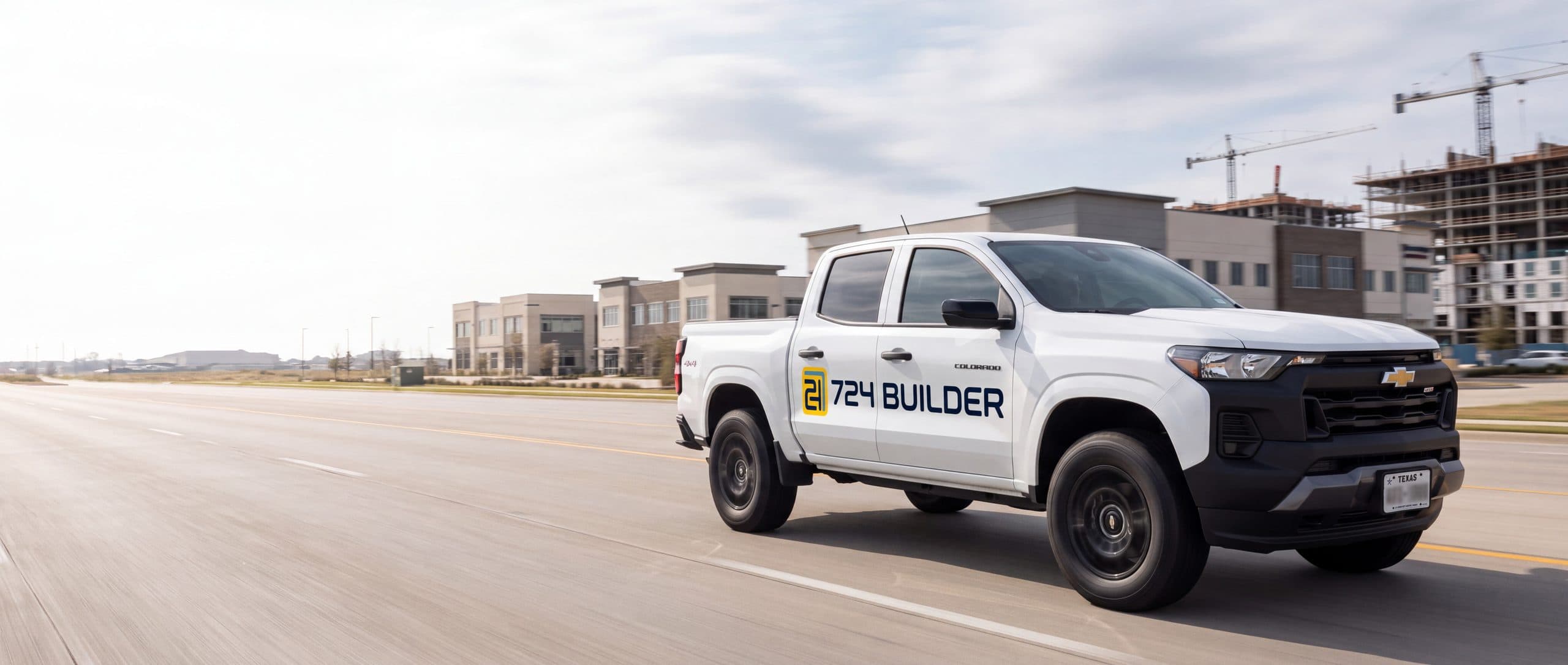 A 724 Builder pickup on the road through a Texas city, buildings under construction behind it.